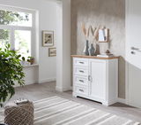 Weiße Kommode mit Holzplatte und vier Schubladen, seitliche Perspektive, dekoriert mit Vasen und Büchern, in einem hellen Raum mit Pflanzen und Wandkunst.