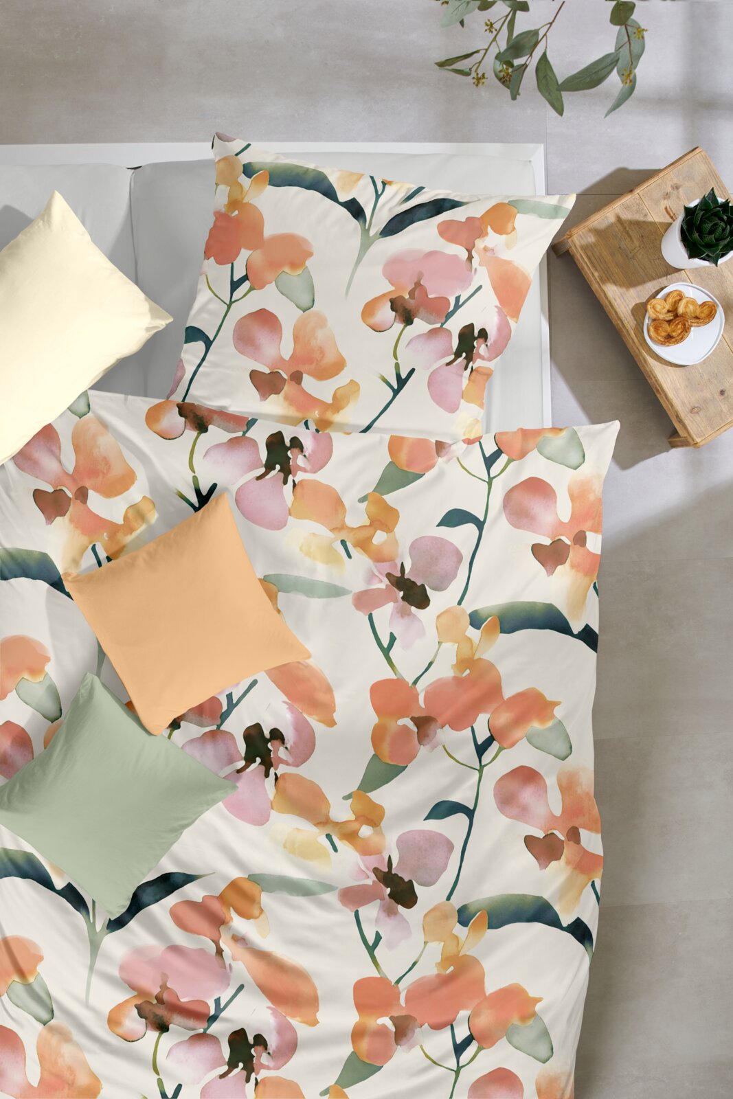 Bettwäsche-Set mit großflächigem Aquarell-Blumenmuster in Orange, Rosa und Grün auf weißem Stoff, Draufsicht von oben auf das gemachte Bett
