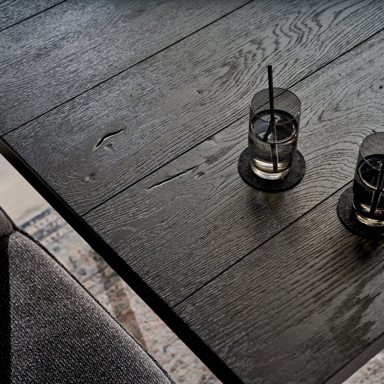 Nahaufnahme eines schwarzen Esstisches aus Holz mit zwei Gläsern Wasser, von oben fotografiert.