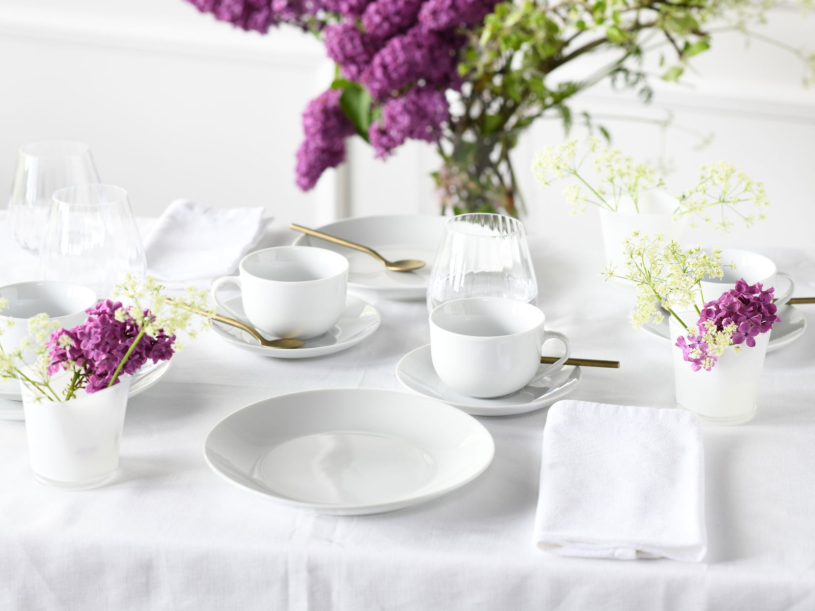 Elegantes weißes Kaffeeservice für 18 Personen, arrangiert auf einem Tisch mit lila und weißen Blumen, aus der Vogelperspektive fotografiert.