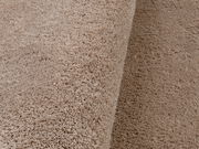 Nahaufnahme eines weichen, beigen Teppichs mit flauschiger Textur, seitliche Perspektive.