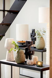 Teelicht in mattem Design auf einem Tisch, umgeben von dekorativen Vasen und Skulpturen, seitliche Perspektive