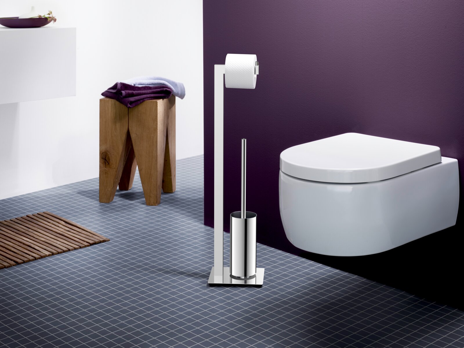 Freistehende WC-Garnitur aus poliertem Edelstahl mit Toilettenpapierhalter und WC-Bürste neben wandhängendem WC im modernen Bad, seitliche Frontansicht