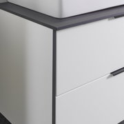 Close-up van een moderne wastafelcombinatie met een witte kast en een donker werkblad, gezien vanaf de zijkant