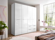 Moderner weißer Kleiderschrank mit hochglänzenden Fronten, mehreren Türen und Schubladen im hellen Schlafzimmer, fotografiert in leichter Front-Links-Perspektive.