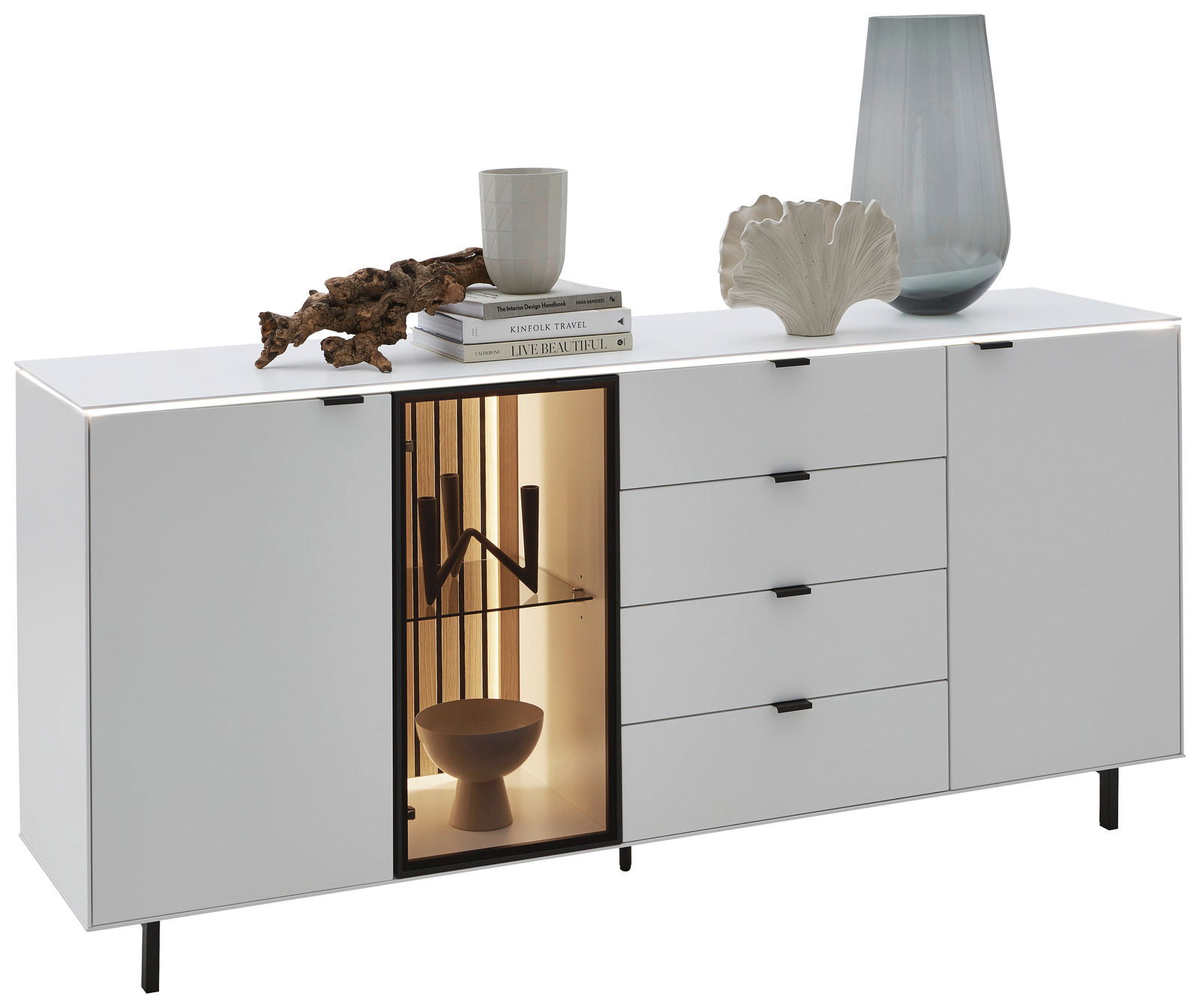 Dieter Knoll Dressoir RIANI Modernes weißes Sideboard mit vier Schubladen und zwei Türen, eine davon mit Glas und Beleuchtung. Dekoriert mit Büchern, einer Vase und einer Skulptur. Perspektive von vorne.