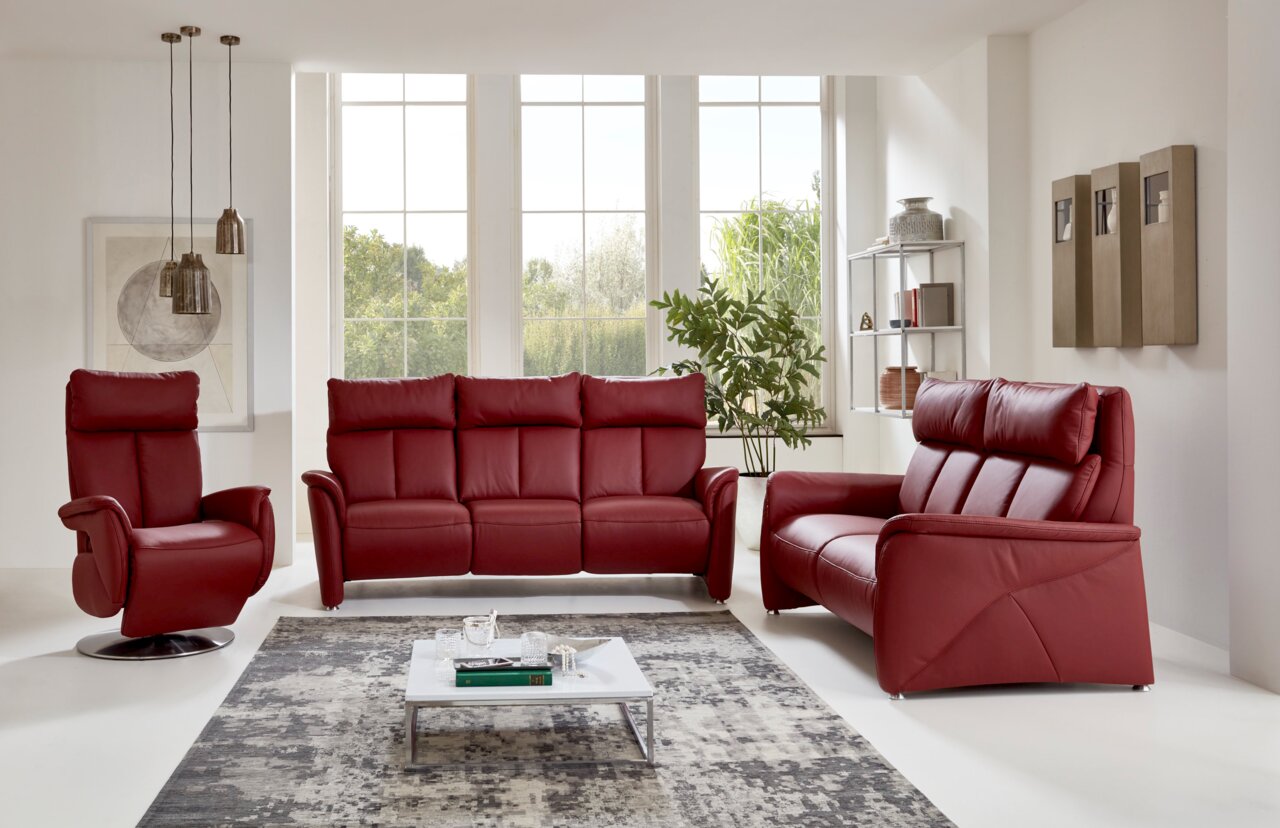 Rotes Ledersofa-Set in modernem Wohnzimmer, bestehend aus einem Sessel, einem Dreisitzer und einem Zweisitzer, mit Blick auf große Fenster im Hintergrund.
