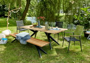 Gartenmöbel-Set bestehend aus einem Holztisch mit Metallbeinen, zwei Stühlen und einer Bank, aufgestellt auf einer grünen Wiese mit Blick auf einen Teich im Hintergrund.