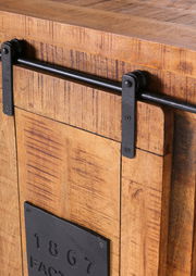 Nahaufnahme eines rustikalen Barschrankes aus Holz mit schwarzem Metallschiebemechanismus und dekorativer Metallplatte mit der Aufschrift '1867'.