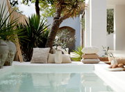 Ein stilvolles Kissen aus Bouclé-Stoff in einer entspannten Outdoor-Umgebung neben einem Pool, umgeben von grünen Pflanzen und einem modernen Dekor.