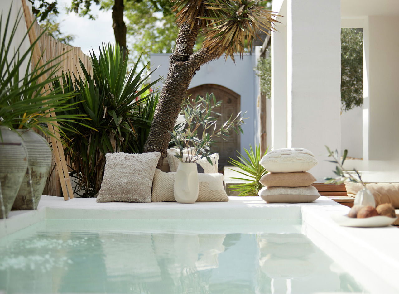 Ein stilvolles Kissen aus Bouclé-Stoff in einer entspannten Outdoor-Umgebung neben einem Pool, umgeben von grünen Pflanzen und einem modernen Dekor.