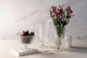 Eine elegante Glasschale auf Fuß, gefüllt mit Trauben, präsentiert aus einer seitlichen Perspektive auf einem Tisch.