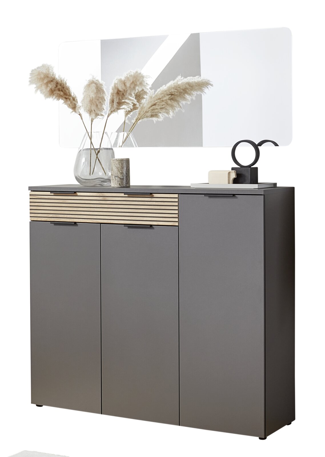 Voleo Garderoben-Set INDO Modernes graues Sideboard mit Holz-Lamellenfront und zwei Türen sowie Schublade, darauf Deko und dahinter ein großer Spiegel; Ansicht frontal leicht von rechts.