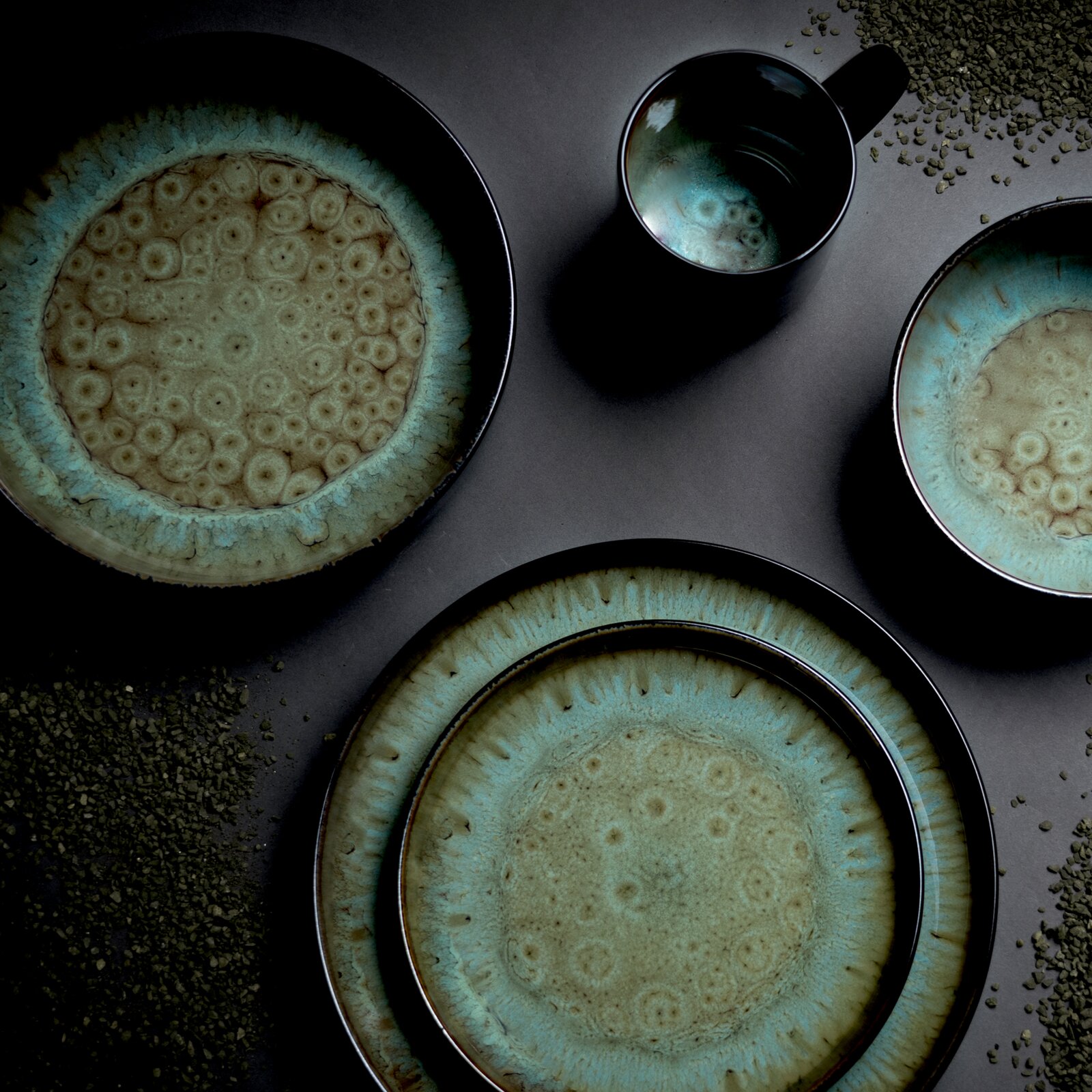 Keramikgeschirr-Set in Blau-Grün mit Teller, Schalen und Becher mit reaktiver Glasur, Draufsicht von oben auf grauem Hintergrund