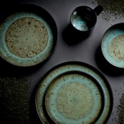 Keramikgeschirr-Set in Blau-Grün mit Teller, Schalen und Becher mit reaktiver Glasur, Draufsicht von oben auf grauem Hintergrund