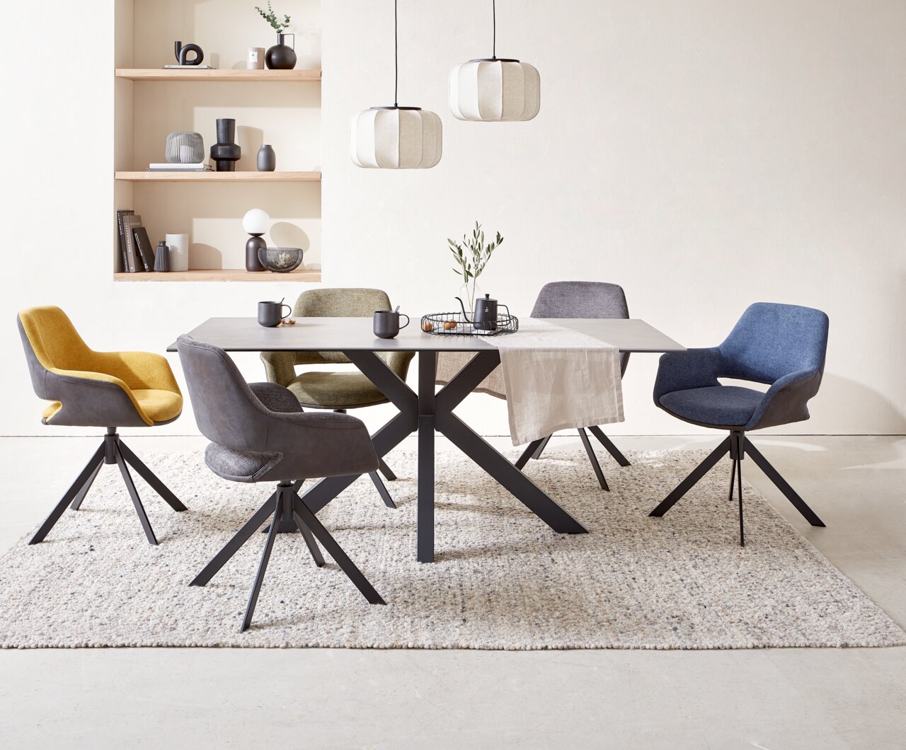 Novel Eettafel CLOUD Moderne eettafel met een zwart metalen onderstel en een lichtgekleurd tafelblad, omringd door kleurrijke stoelen in een stijlvolle eetkamer, gezien vanuit de zijkant.