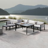 Moderne Lounge-Möbel auf einer Terrasse mit Seeblick, bestehend aus einem Ecksofa, einem Gartentisch und einem Beistelltisch, von vorne betrachtet.