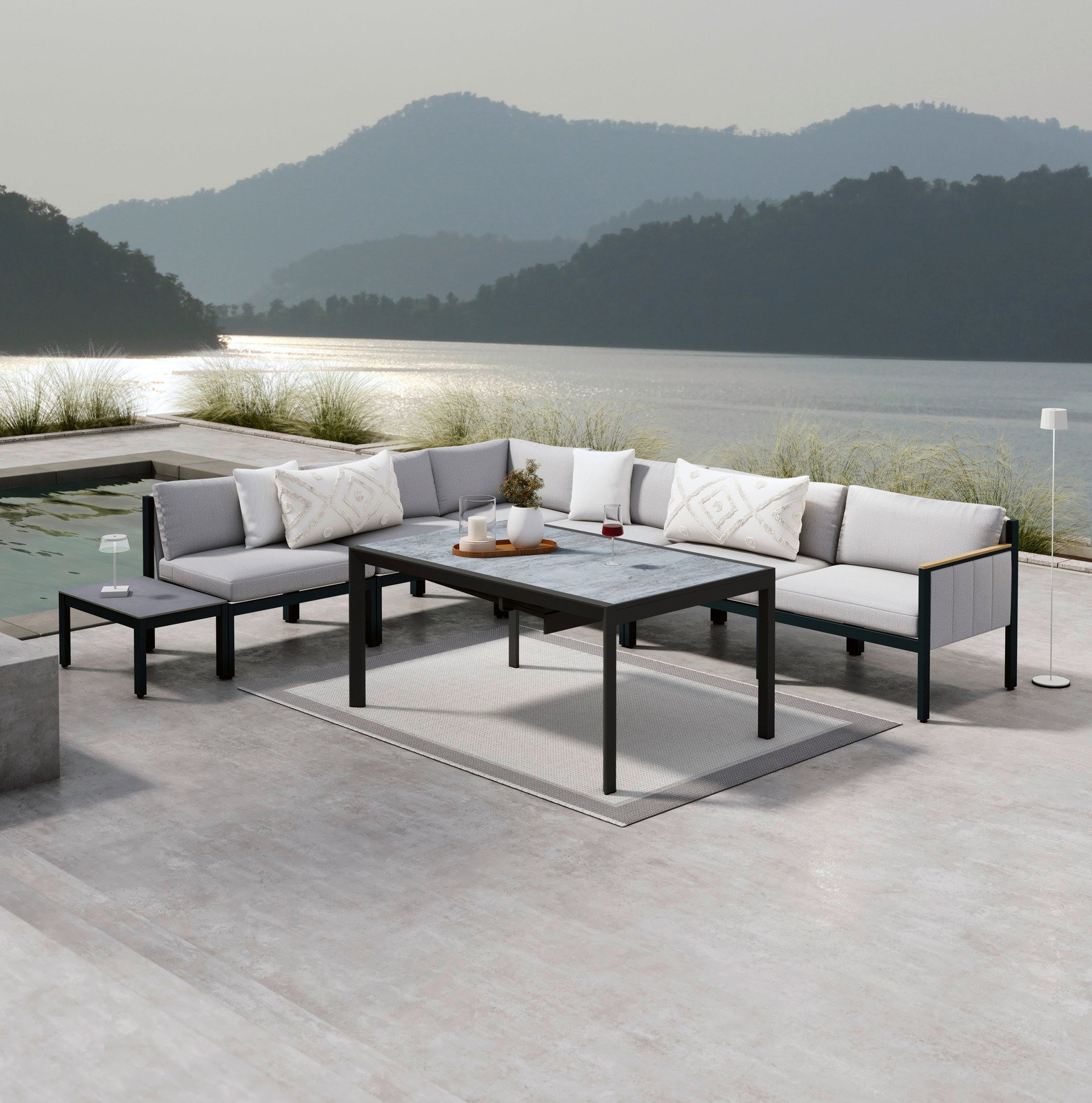 Moderne Lounge-Möbel auf einer Terrasse mit Seeblick, bestehend aus einem Ecksofa, einem Gartentisch und einem Beistelltisch, von vorne betrachtet.