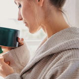 Nahaufnahme einer Person in einem beigen Kapuzenbademantel, die eine Tasse hält, seitliche Perspektive.