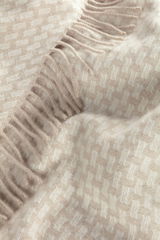 Nahaufnahme eines weichen Plaids mit Fransen und einem dezenten geometrischen Muster in Beige- und Cremetönen.