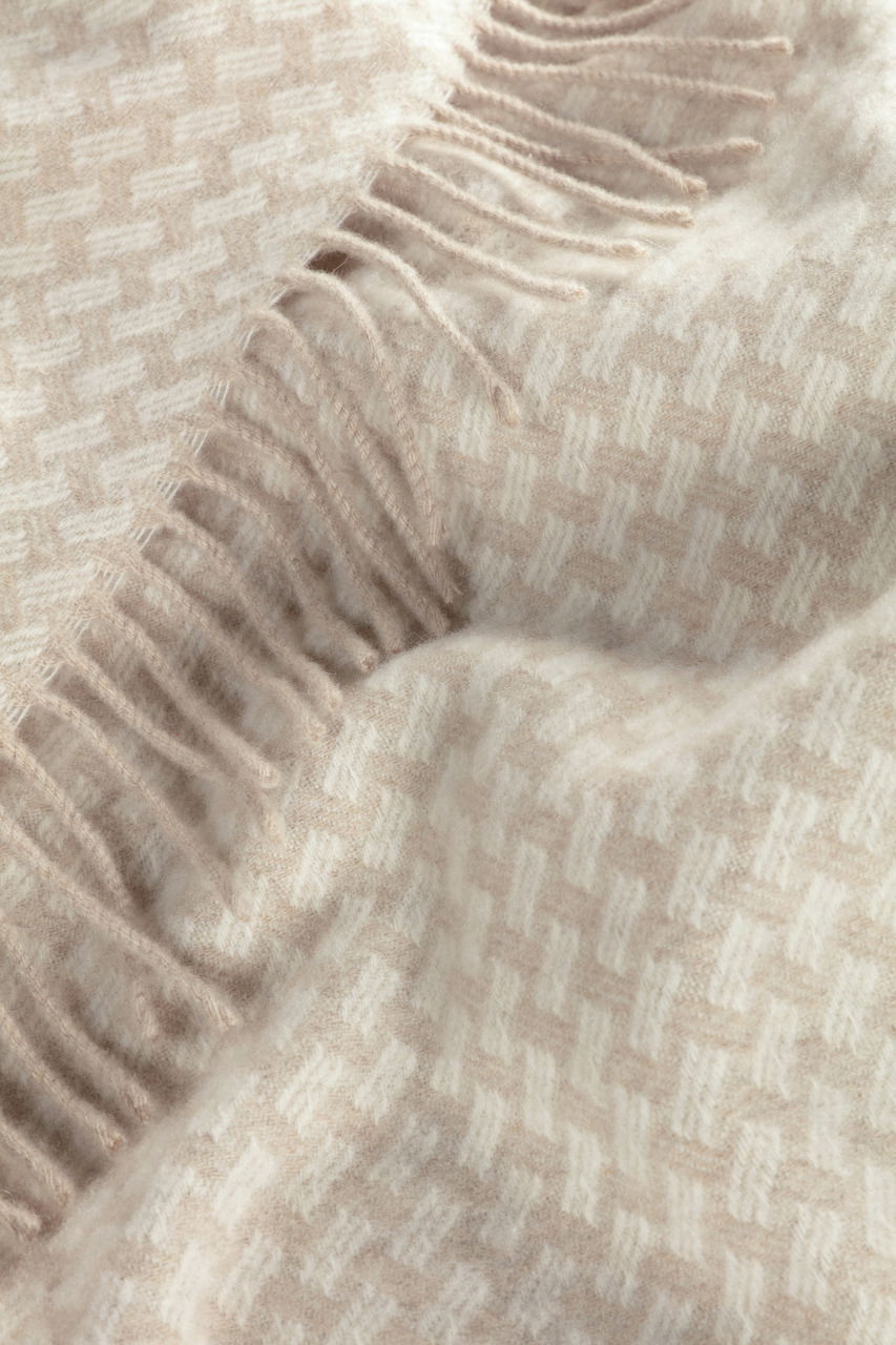 Nahaufnahme eines weichen Plaids mit Fransen und einem dezenten geometrischen Muster in Beige- und Cremetönen.