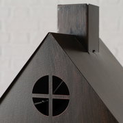 Nahaufnahme eines dekorativen, dunkel gebeizten Holzhauses mit rundem Fenster und Schornstein, fotografiert aus leicht seitlicher Frontperspektive vor hellem Hintergrund.