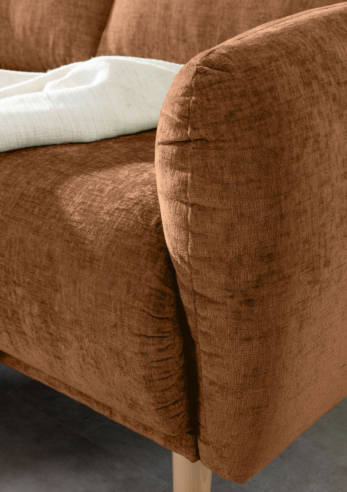 Nahaufnahme einer braunen Sofaecke mit abgerundeter Armlehne und einem weißen Tuch, Perspektive von der Seite.