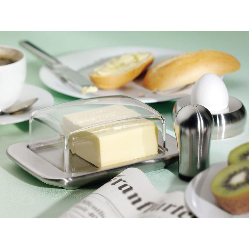 Butterdose LOFT aus Edelstahl mit transparentem Deckel, präsentiert auf einem gedeckten Frühstückstisch mit Brötchen, Ei und Kaffee. Perspektive von schräg oben.