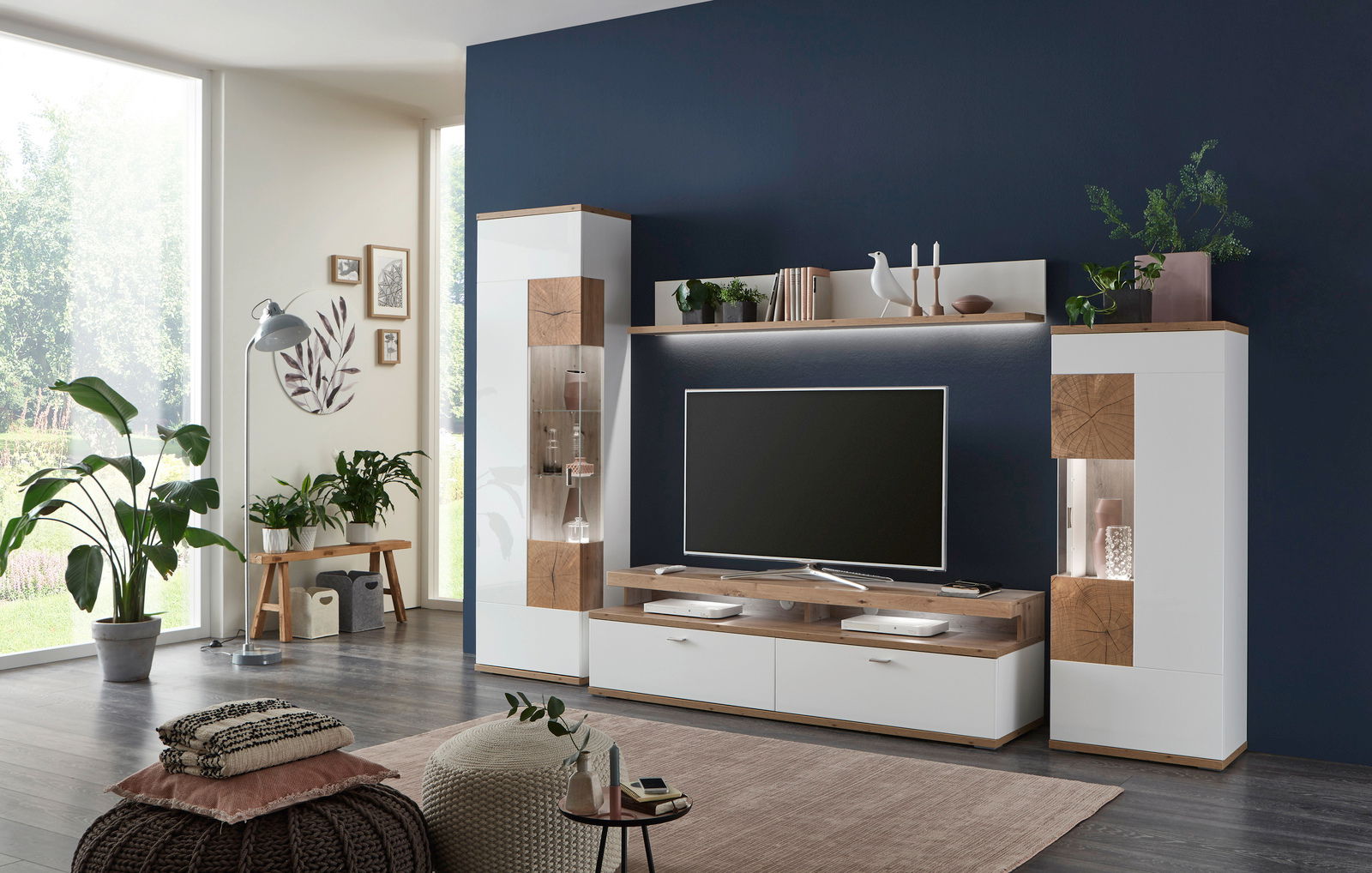 Moderne Wandkombination SYLT in einem stilvollen Wohnzimmer, frontal betrachtet. Die Kombination aus weißen und holzfarbenen Elementen bietet Platz für Dekoration und Unterhaltungselektronik.