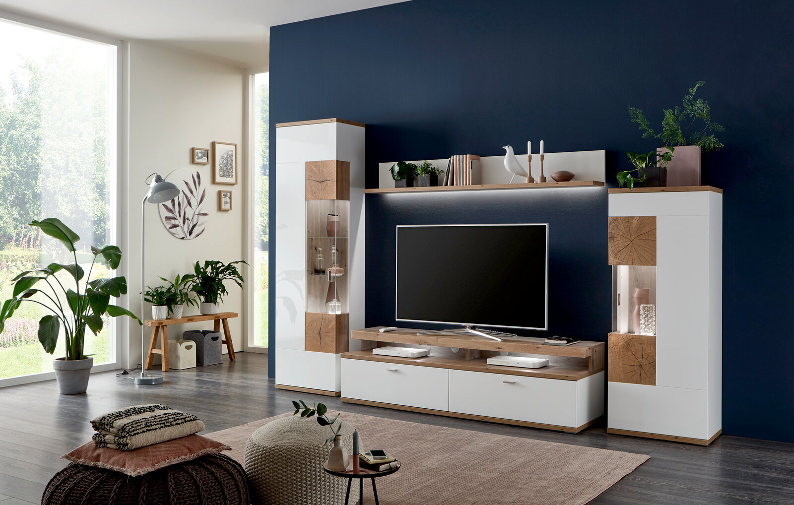 Moderne Wandkombination SYLT in einem stilvollen Wohnzimmer, frontal betrachtet. Die Kombination aus weißen und holzfarbenen Elementen bietet Platz für Dekoration und Unterhaltungselektronik.