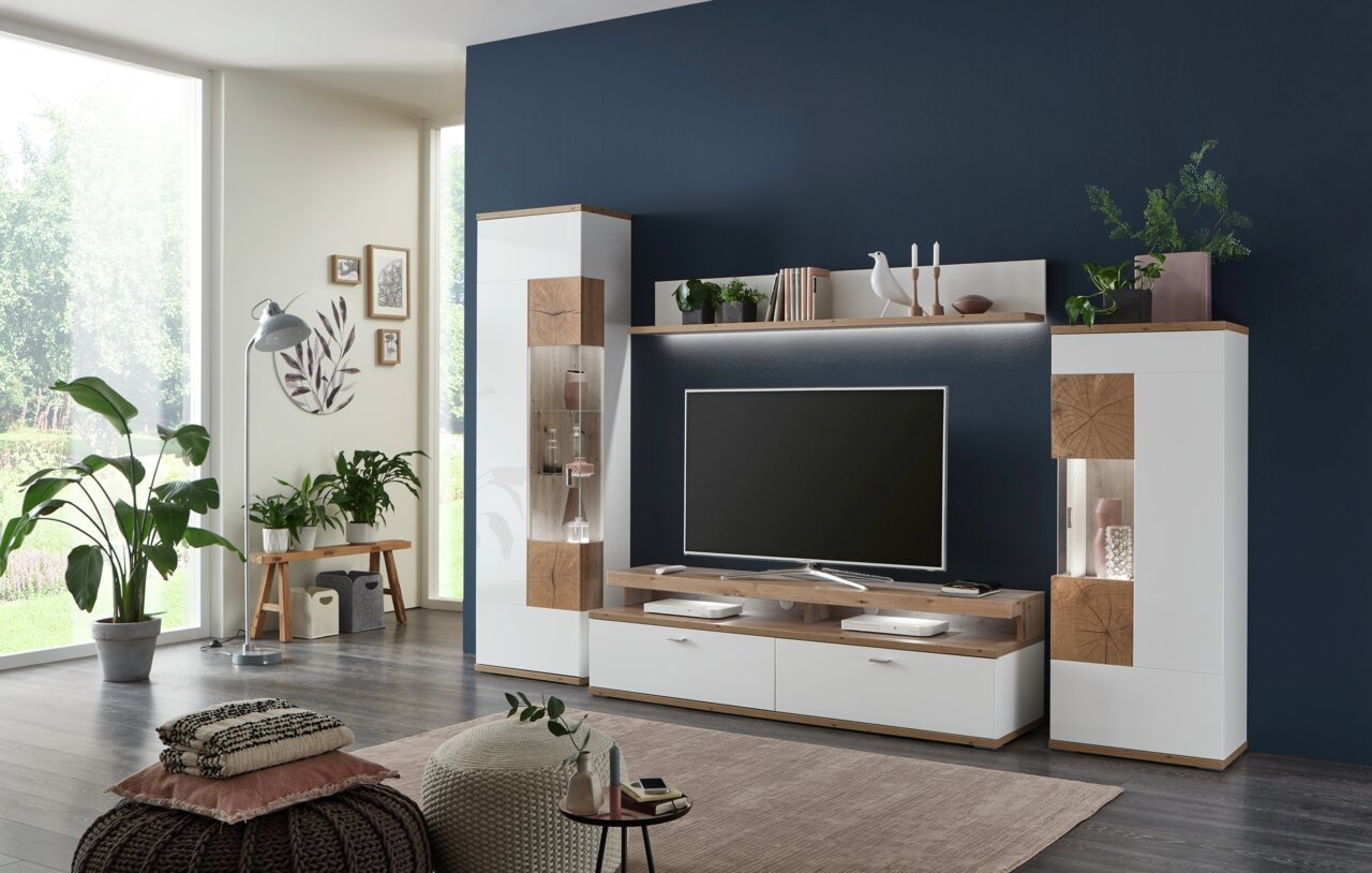 Moderne Wandkombination SYLT in einem stilvollen Wohnzimmer, frontal betrachtet. Die Kombination aus weißen und holzfarbenen Elementen bietet Platz für Dekoration und Unterhaltungselektronik.