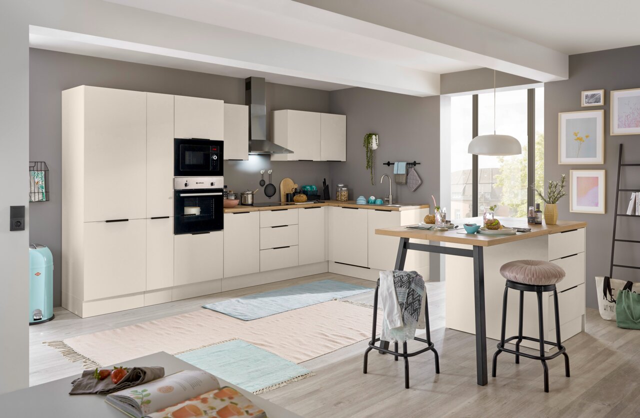 Moderne L-förmige Einbauküche in Cremeweiß mit Holzarbeitsplatte, integrierten Backofen und Mikrowelle, Dunstabzugshaube sowie Kücheninsel mit Barhockern Perspektive: frontale Weitwinkelansicht leicht von links.
