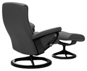 Achterkant van een moderne, grijze fauteuil met bijpassende voetenbank, beide op een zwart, rond onderstel.