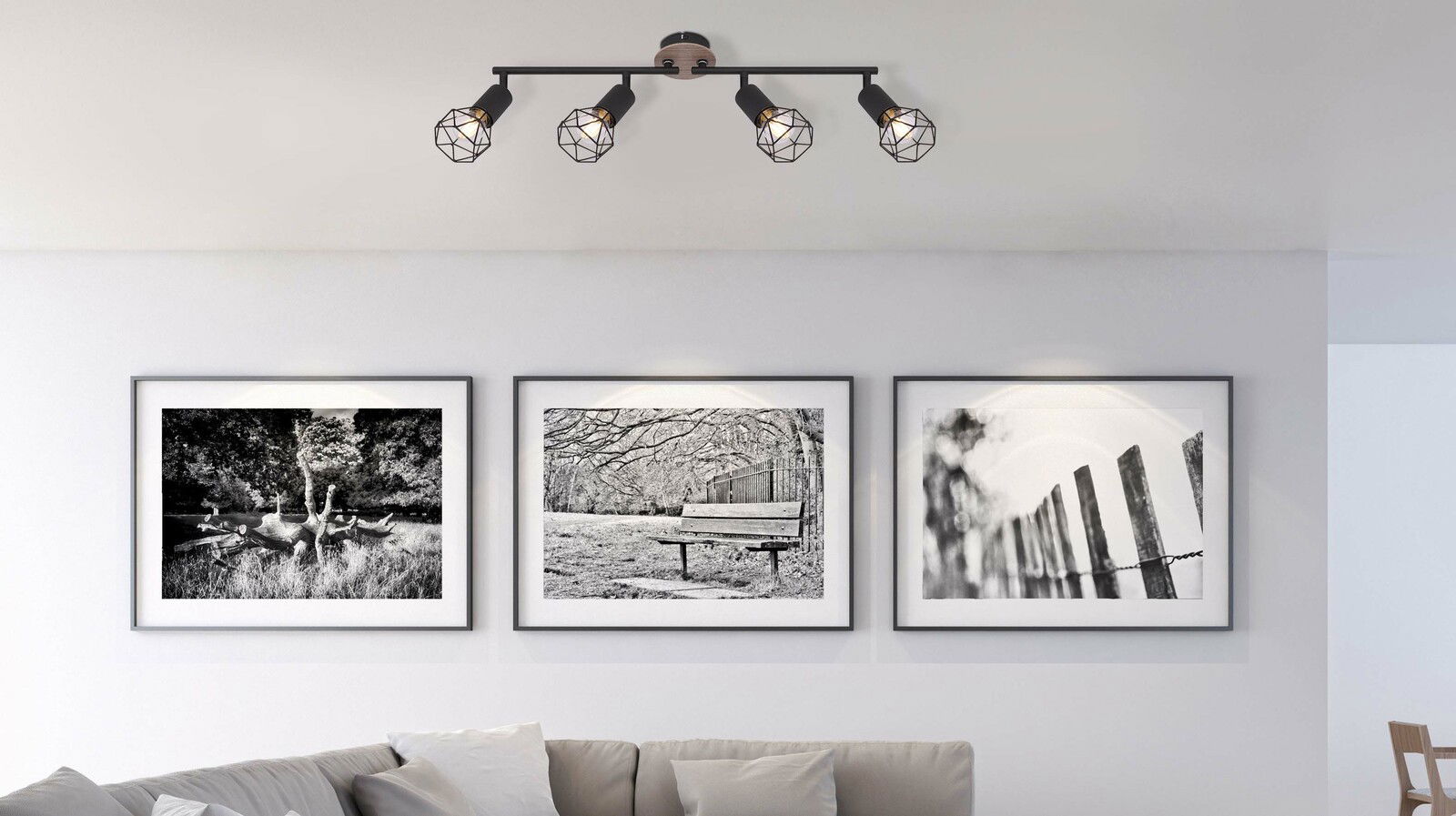 Deckenstrahler XARA I mit vier schwarzen, geometrischen Lampenschirmen, montiert an der Decke eines modern eingerichteten Wohnzimmers. Perspektive von unten, zeigt die Beleuchtung über einer Bildergalerie.