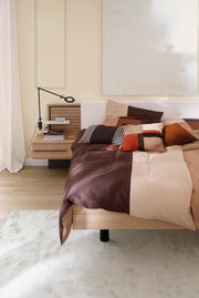 Satin-Bettwäsche 155x220 cm in einem modernen Schlafzimmer, mit einem Patchwork-Design in warmen Erdtönen, aus der Perspektive von der Seite des Bettes.
