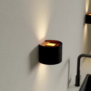 Moderne schwarze Wandlampe mit warmweißem Up-and-Down-Lichtkegel an heller Wand, Nahaufnahme in seitlicher Perspektive (schräg von vorn).