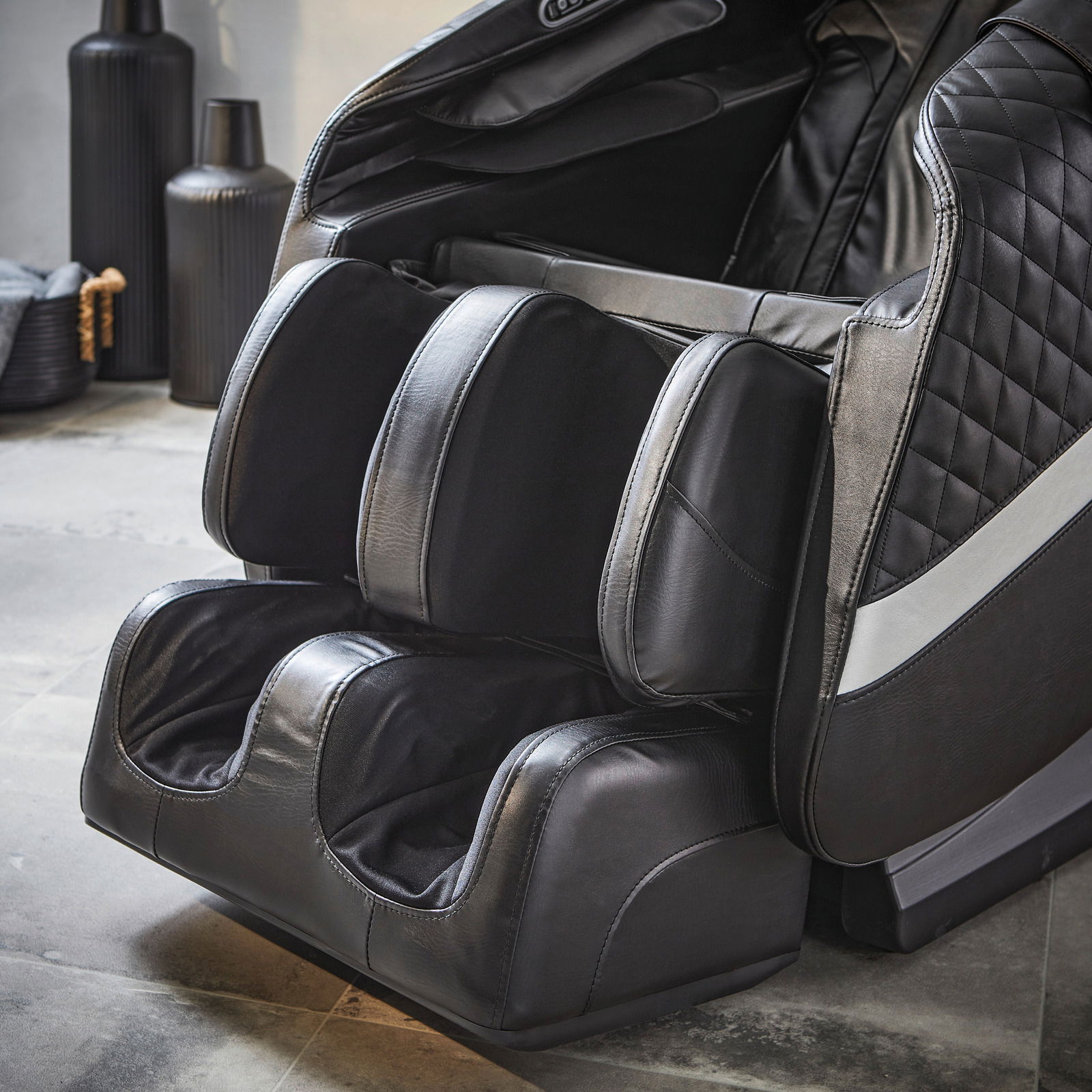Nahaufnahme eines luxuriösen Massagesessels in schwarzem Leder mit Fuß- und Beinmassagefunktion, seitliche Perspektive.