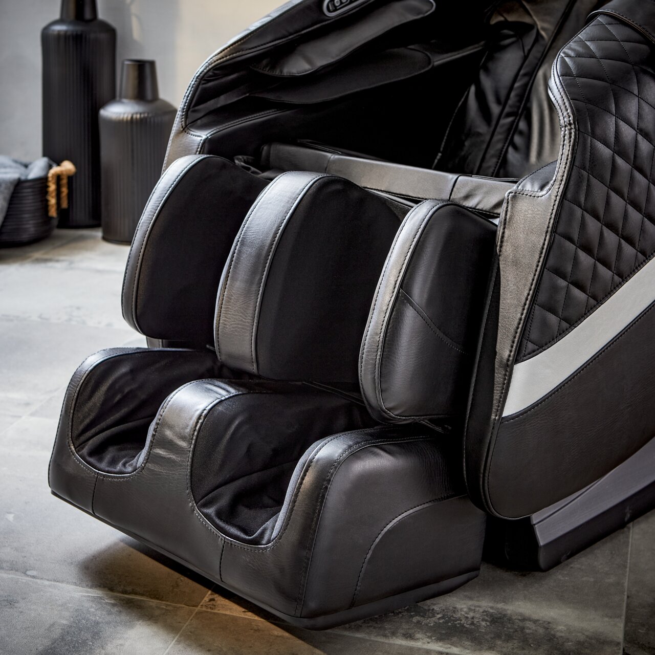 Nahaufnahme eines luxuriösen Massagesessels in schwarzem Leder mit Fuß- und Beinmassagefunktion, seitliche Perspektive.