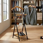 Kleiderständer im Leiter-Design mit Holzstange und schwarzem Metallgestell, vorne in 3/4-Ansicht; daran hängt ein graues Sakko auf einem Bügel, unten steht ein Paar schwarze Lederschuhe, im Hintergrund ein begehbarer Kleiderschrank.