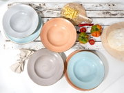 Pastellfarbene Keramik-Speiseteller in Blau, Rosa und Grau mit gesprenkelter Glasur auf rustikalem Holztisch, Draufsicht (Flatlay) mit Nudeln, Tomaten und Teig