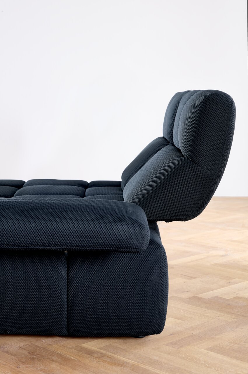 Zijaanzicht van een moderne, donkergrijze hoekbank met verstelbare rugleuning op een houten vloer.