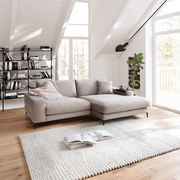 Beige Longchairkombination in einem modernen Wohnzimmer mit Dachschräge, Holzboden und großen Fenstern, seitliche Perspektive.