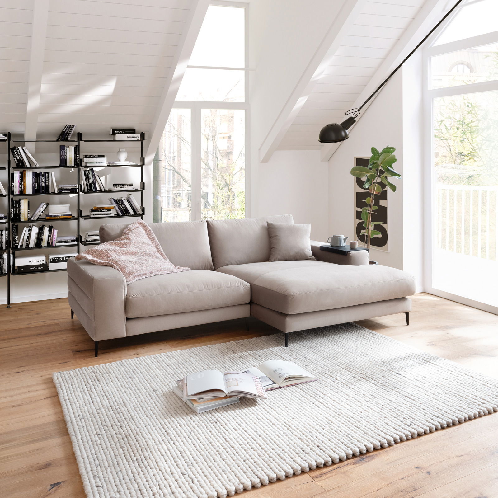 Beige Longchairkombination in einem modernen Wohnzimmer mit Dachschräge, Holzboden und großen Fenstern, seitliche Perspektive.