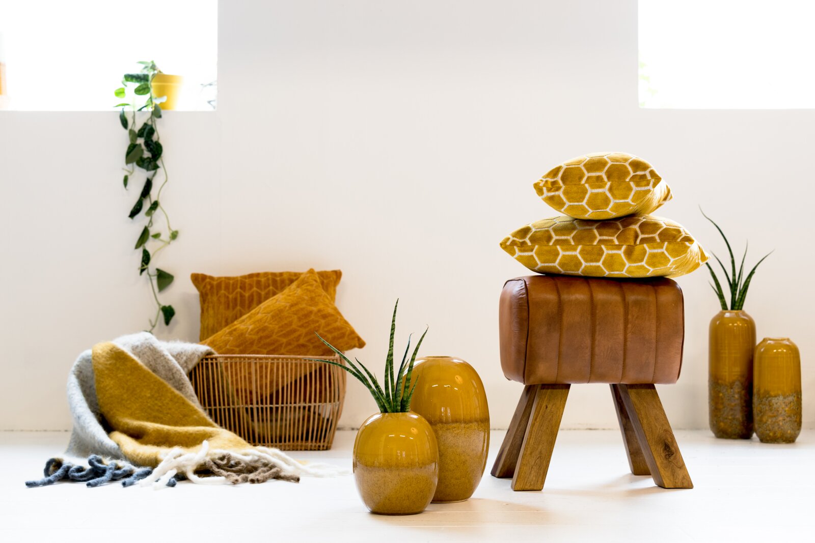 Moderner Hocker aus braunem Leder mit Holzbeinen, im Vordergrund mit gelben Kissen und Vasen dekoriert, seitliche Perspektive.