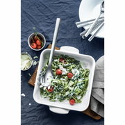 Een Nuova-pastalepel in een witte ovenschaal met spinaziepasta en cherrytomaatjes, van bovenaf gefotografeerd.