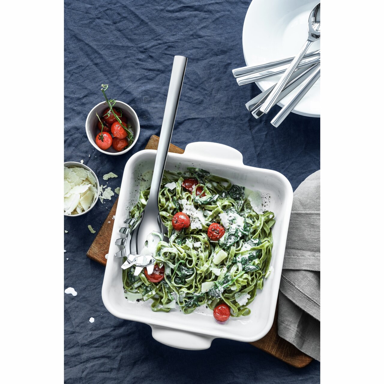 Een Nuova-pastalepel in een witte ovenschaal met spinaziepasta en cherrytomaatjes, van bovenaf gefotografeerd.