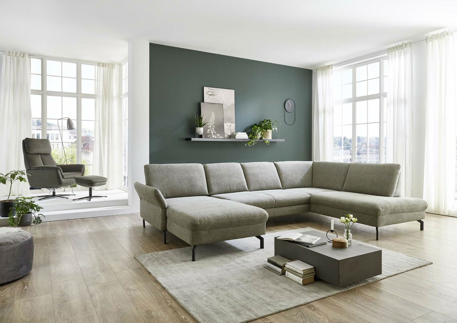 Moderne Polsterrundecke in einem hellen Wohnzimmer mit großen Fenstern, grauem Teppich und Couchtisch, seitliche Perspektive.