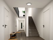 Moderner Hausflur mit grauer Treppe, weißen Türen und runder Deckenleuchte, frontal aus Augenhöhe aufgenommen.