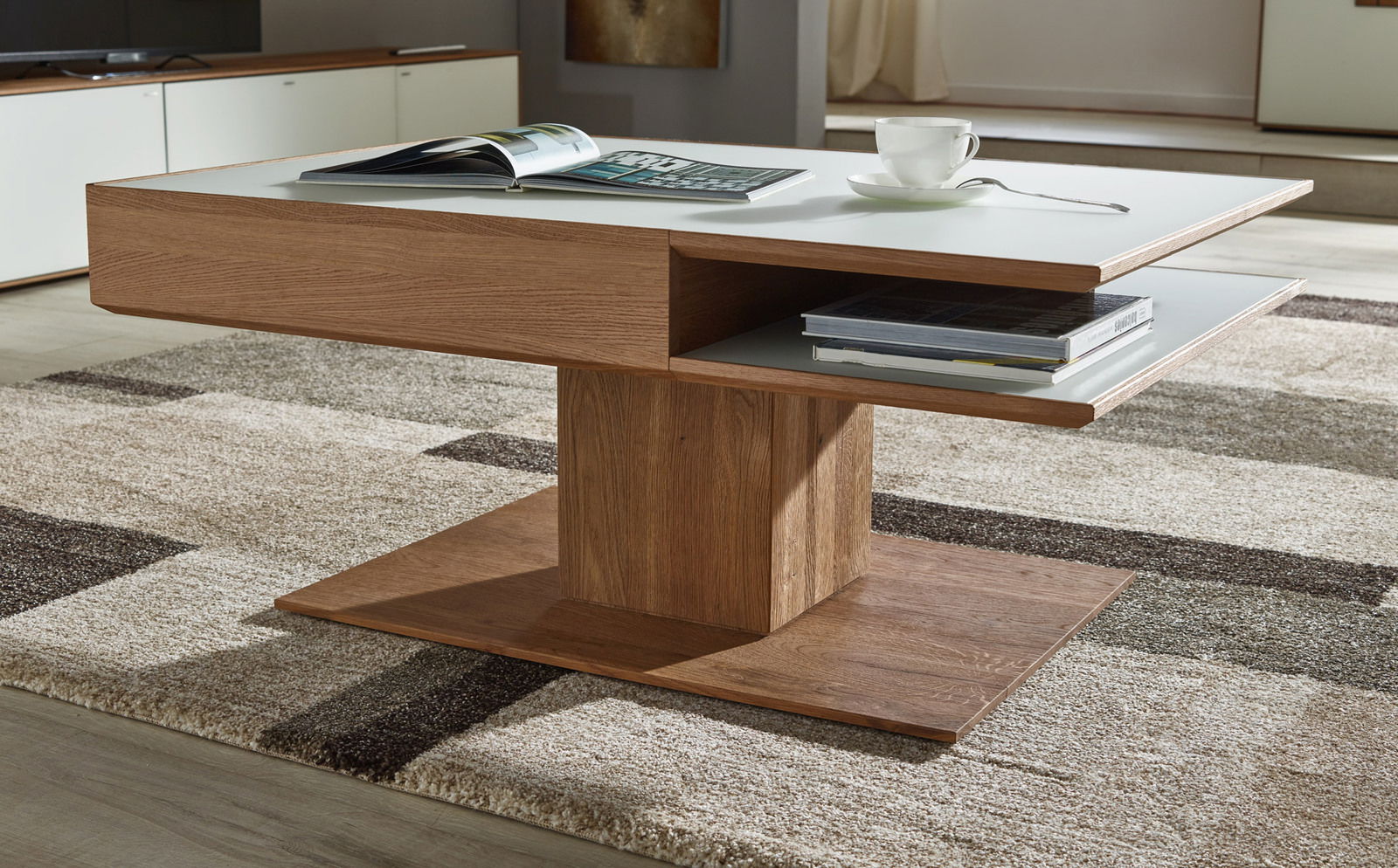 Moderner Couchtisch aus Holz mit weißer Tischplatte, seitlicher Perspektive, auf einem Teppich stehend, mit Büchern und einer Tasse darauf.