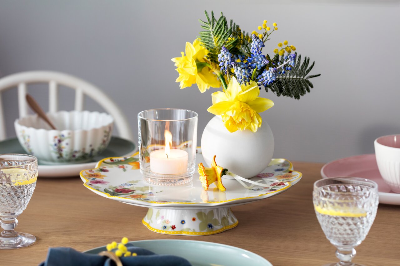 Ein elegant gedeckter Tisch mit einem Wasserglas Boston im Vordergrund, umgeben von Geschirr und einer Blumenvase. Perspektive: seitlich.